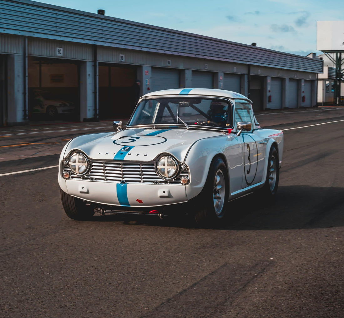 Classic Triumph TR4 race car on track at HPDE event garage area.