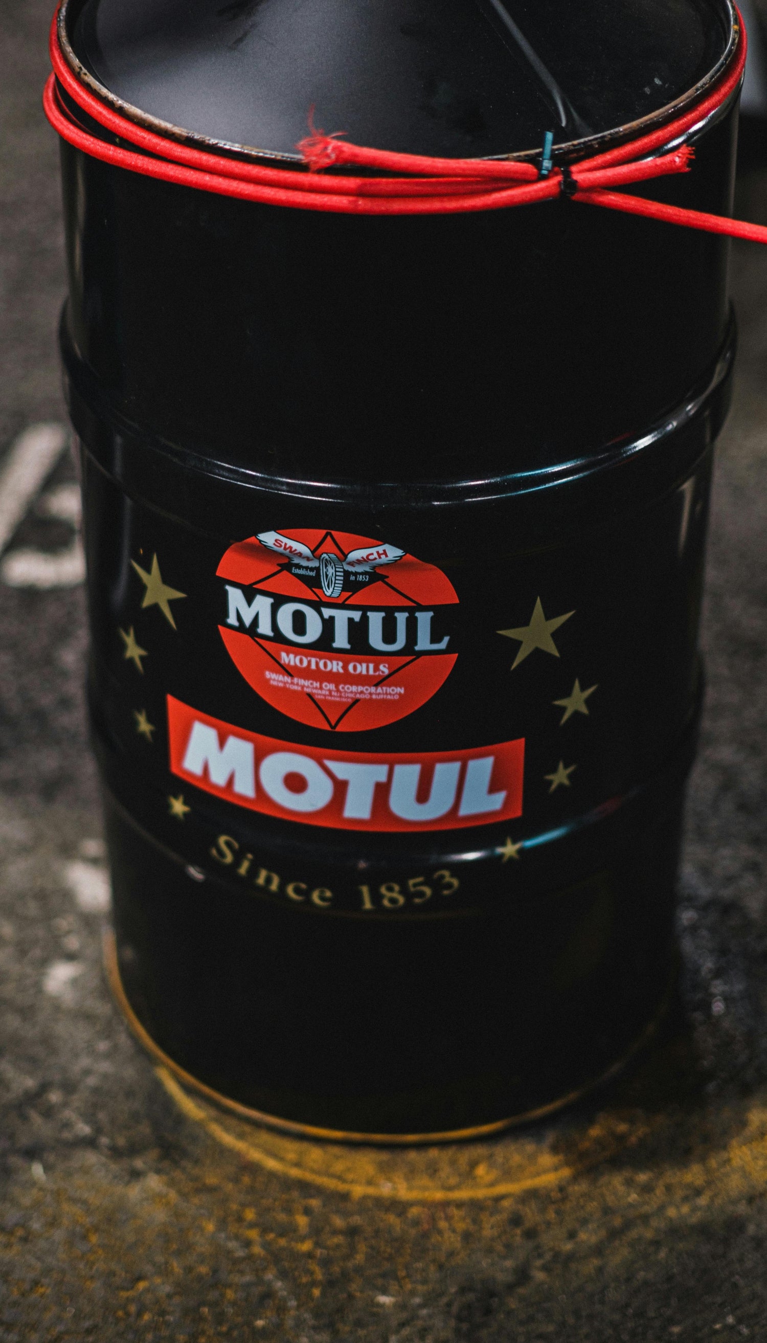 Black Motul motor oil drum with red logo representing fluids collection products.
